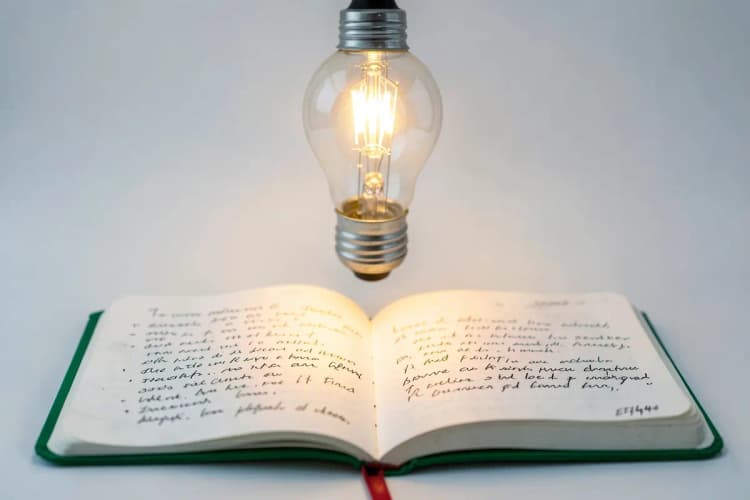 Lâmpada acesa sobre um bloco de notas com ideias escritas.