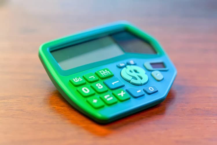 Uma calculadora mostrando o número 0 ao lado de um ícone de cifrão, sobre um fundo de madeira.