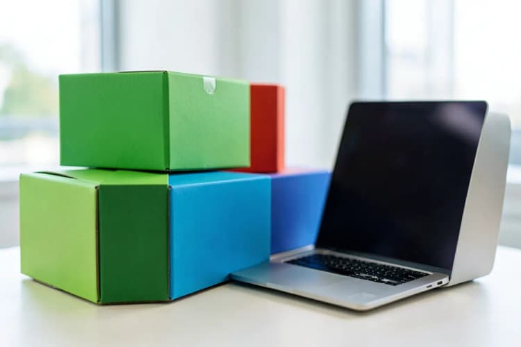 Caixas de diferentes tamanhos empilhadas em frente a um laptop aberto, sugerindo a logística de vendas online.