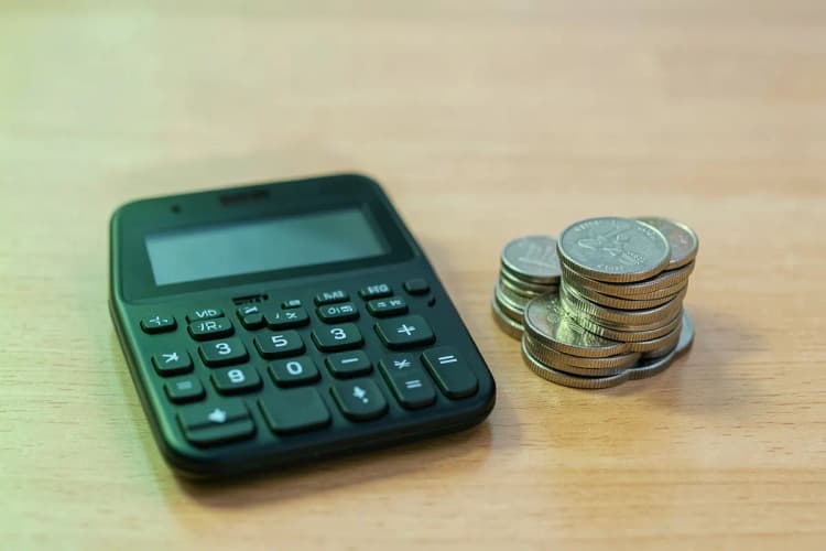 Uma calculadora e moedas empilhadas, representando o custo e o investimento em um sistema.